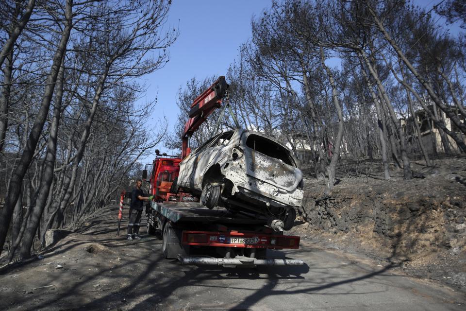 A worker transports a burnt car following a wildfire in Neos Voutzas, east of Athens, Friday, July 27, 2018. Greek authorities said Thursday there were serious indications that a deadly wildfire that gutted a vacation resort near Athens was started deliberately, while experts warned that the devastated coastal town had been built like a "fire trap," with poor safety standards and few escape routes. (AP Photo/Thanassis Stavrakis)