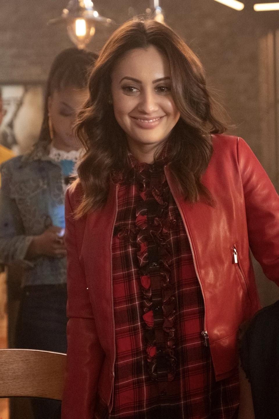 Woman in a red jacket and plaid skirt smiling in an indoor setting