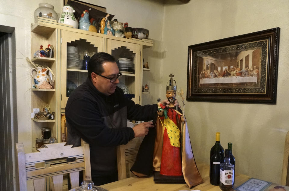 Mayordomo Fidel Trujillo adjusts the cape on his bulto, or wooden sculpture of St. Joseph, that's kept for safekeeping at his aunt's home in Ledoux, New Mexico, Saturday, April 15, 2023. Each mission church is devoted to a particular saint, for whom the community develops such veneration that the image is sometimes kept at the home of mayordomos for safekeeping and easier access. (AP Photo/Giovanna Dell'Orto)