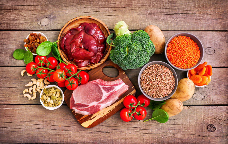 Iron sources on wooden background: liver, beef, raisins, keshew, spinach, tomatoes, potatoes, buckwheat, pumpkin seeds, lentil, broccoli, dried appricots. Top view.