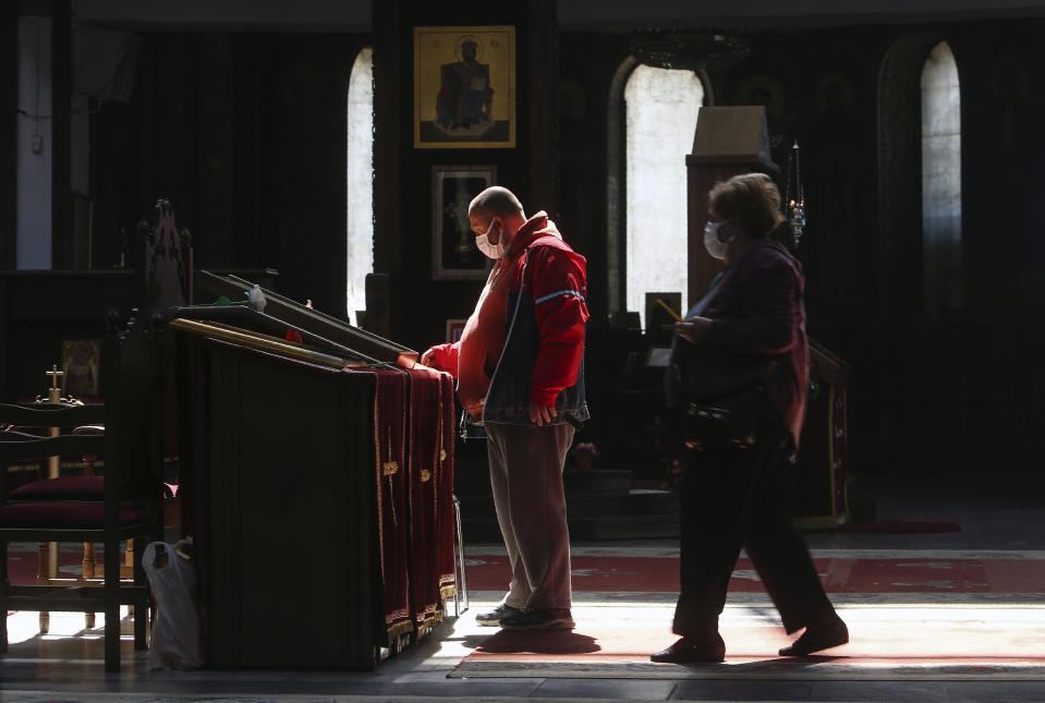 In this Thursday, April 16, 2020, photo, a couple, wearing face masks to protect themselves from the coronavirus, approach an icon in the St. Clement Christian Orthodox Church in Skopje, North Macedonia. For Orthodox Christians, this is normally a time of reflection, communal mourning and then joyful release, of centuries-old ceremonies steeped in symbolism and tradition. But this year, Easter - by far the most significant religious holiday for the world's roughly 300 million Orthodox - has essentially been cancelled. (AP Photo/Boris Grdanoski)