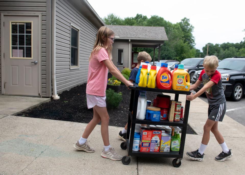 Jan Seljan collected materials and money donated from a Noah's Ark Childcare car wash event for the Haven of Portage County. The class helps carry the donations to Jan Seljan's vehicle.  Reese Begue and Jack Severs move the cart of items down a small incline.