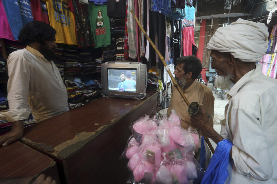 A shopkeeper and passersby watch the cricket World Cup match between Pakistan and India, at a shop in Lahore, Pakistan, Sunday, June 16, 2019. (AP Photo/K.M. Chaudary)