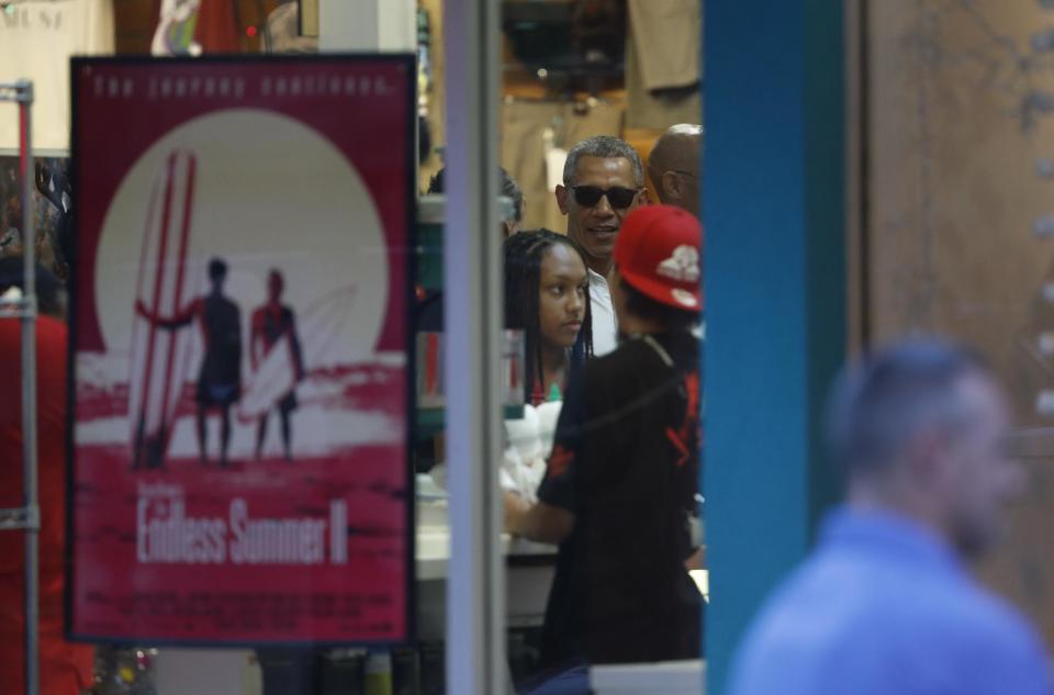 President Barack Obama, wearing sunglasses, is seen through the window of Island Snow Hawaii as he and family and friends order shave ice in Kailua, Hawaii, Saturday, Dec. 24, 2016, during the first family's annual vacation. (AP Photo/Carolyn Kaster)