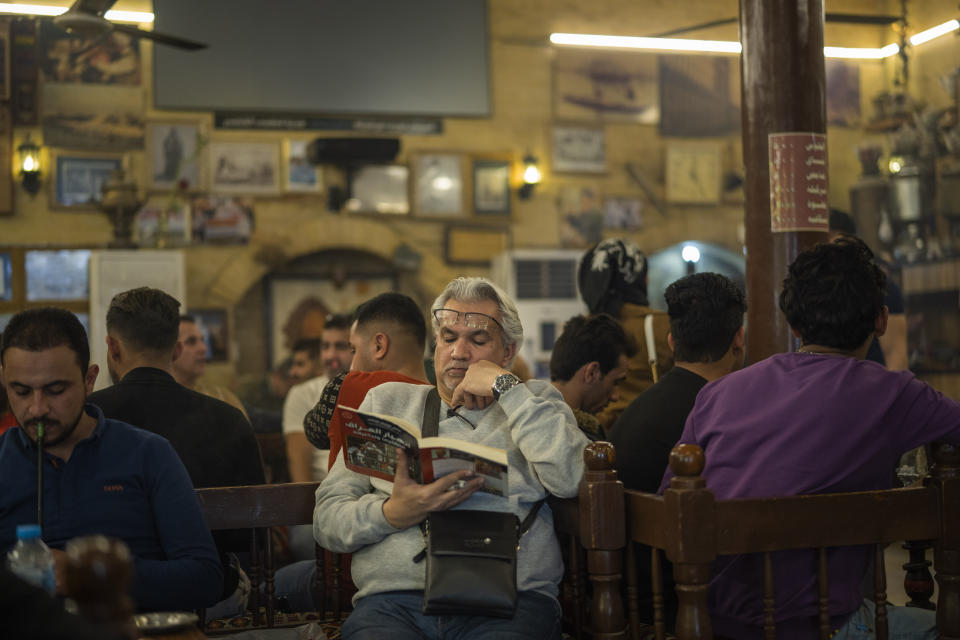 A man reads a book at the Alshabander cafe on Al-Mutanabbi street in Baghdad, Iraq, Friday, Feb. 24, 2023. A U.S.-led war two decades earlier deposed a dictator whose imprisonment, torture and execution of dissenters had kept 20 million people living in fear for a quarter of a century. But it also broke what had been a unified state at the heart of the Arab world. (AP Photo/Jerome Delay)