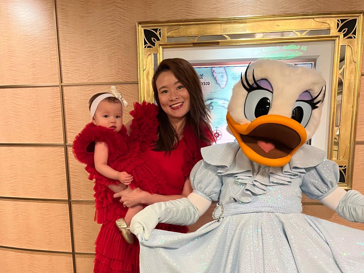 Tiffany Leigh  and her baby wearing a matching red dresses posing for a photo with a duck mascot on a Disney cruise.