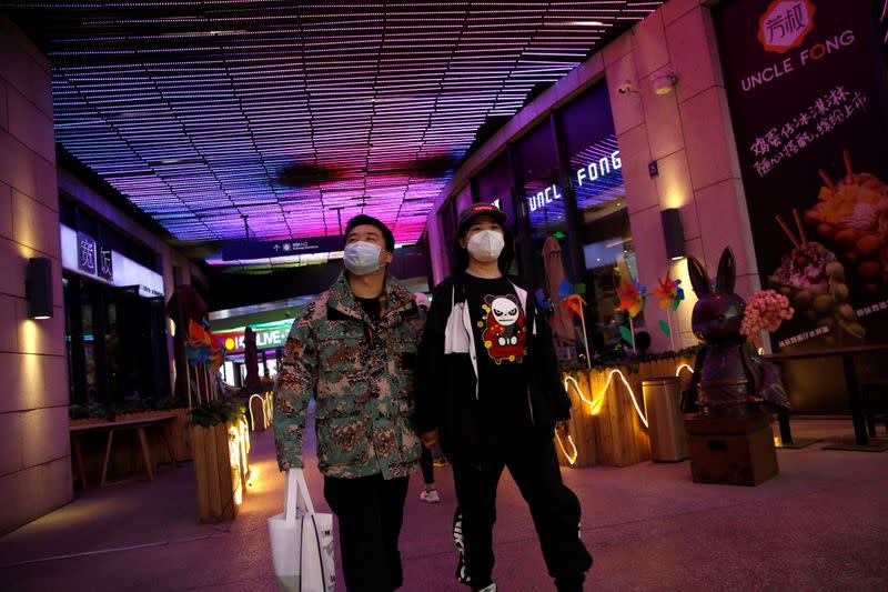 People wearing face masks walk past restaurants at a shopping complex in Beijing