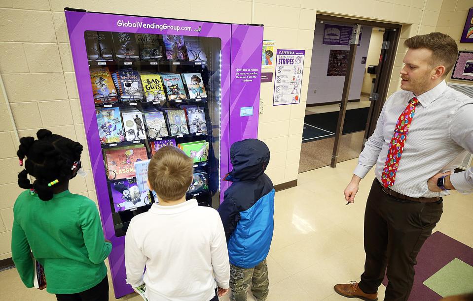 Pickerington Elementary third-graders Erin Ampah, Micah Haverfield and Calvin Brokaw look over the books in the new book vending machine on Feb. 9 as principal Dave Zwiebel watches. The students earned books by receiving a Golden Stripe Award, which recognizes students for positive behavior.