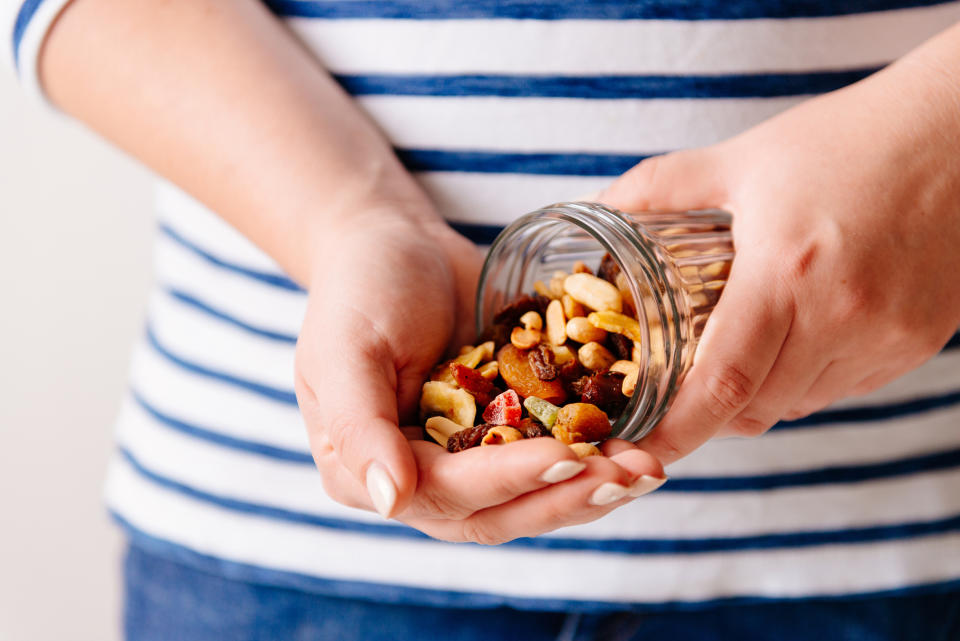 A pair of hands holding an open jar of dried fruits and nuts