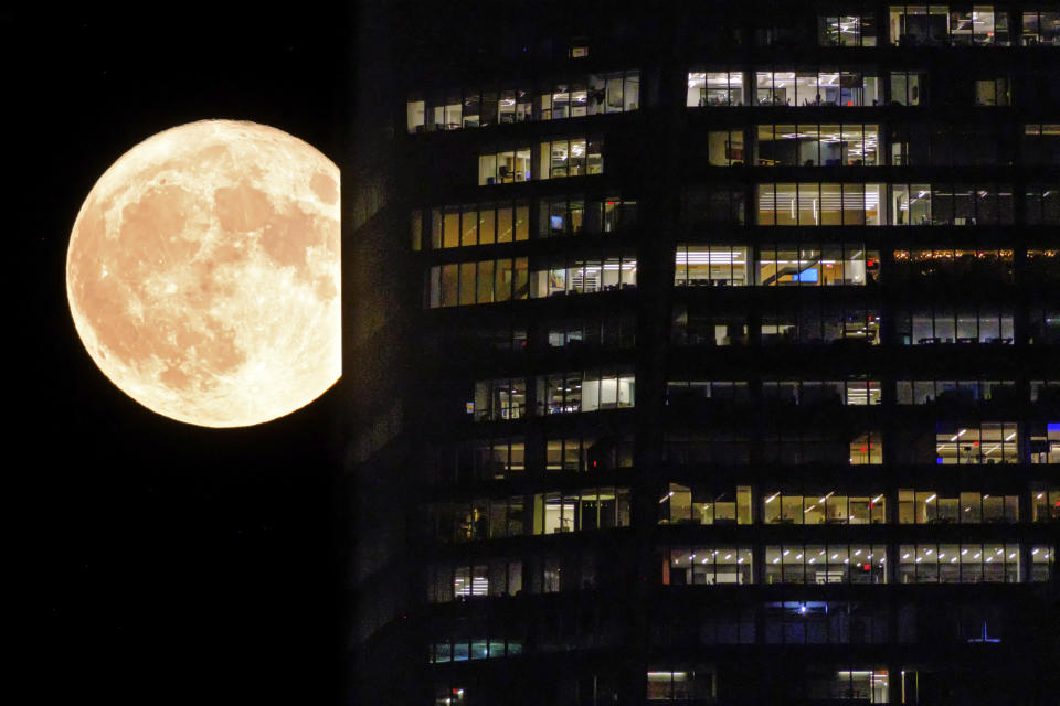 FILE - A supermoon passes behind the illuminated windows of a New York City skyscraper, Aug. 1, 2023. A rare blue supermoon could normal raise tides just as Hurricane Idalia takes aim at Florida’s west coast, exacerbating flooding from the storm. The moon will be closest to the Earth on Wednesday night, Aug. 30, the same day Idalia is expected to make landfall in Florida. (AP Photo/J. David Ake, File)