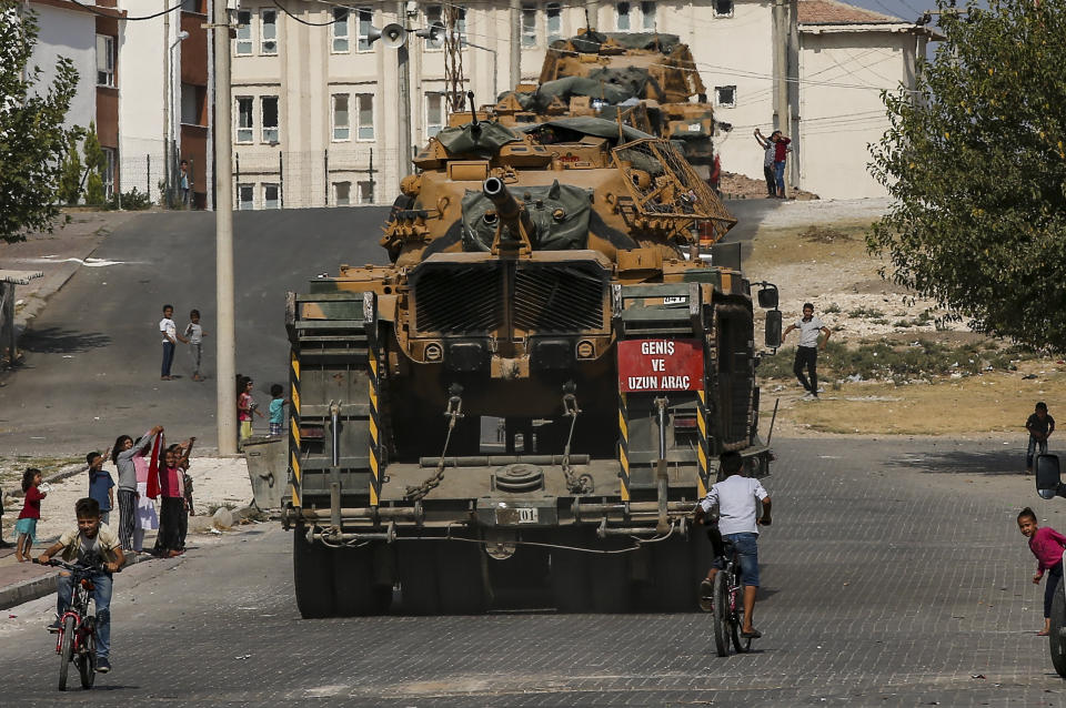 Local residents cheer, as Turkish army tanks are transported on trucks in the outskirts of the town of Akcakale, in Sanliurfa province, southeastern Turkey, at he border of Syria, Thursday, Oct. 17, 2019. U.S. Vice President Mike Pence, heading a delegation that includes Secretary of State Mike Pompeo and White House national security adviser Robert O'Brien, arrived in Turkey on Thursday, a day after Trump dismissed the very crisis he sent his aides on an emergency mission to douse.(AP Photo/Emrah Gurel)