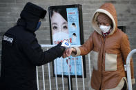 FILE - In this Feb. 16, 2020, file photo, woman wearing a protective face mask receives a temperature check from a security guard as she enters Qianmen Street, a popular tourist spot, in Beijing. As the coronavirus spreads around the world, International health authorities are hoping countries can learn a few lessons from China, namely, that quarantines can be effective and acting fast is crucial. On the other hand, the question before the world is to what extent it can and wants to replicate China’s draconian methods. (AP Photo/Andy Wong, File)