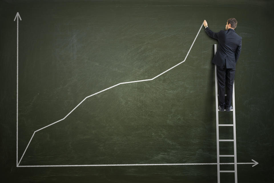 A businessman draws a rising stock chart on a blackboard.