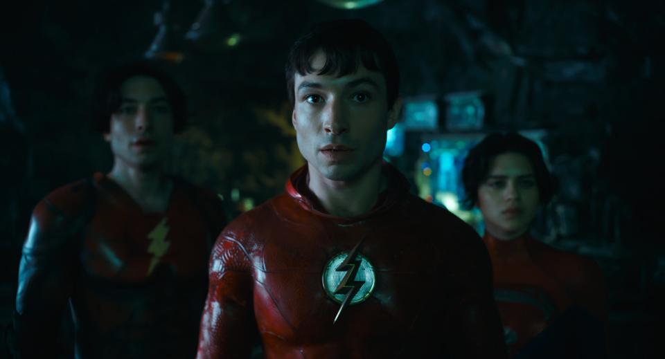 Ezra Miller behind another version of himself as The Flash and Sasha Calle as Supergirl