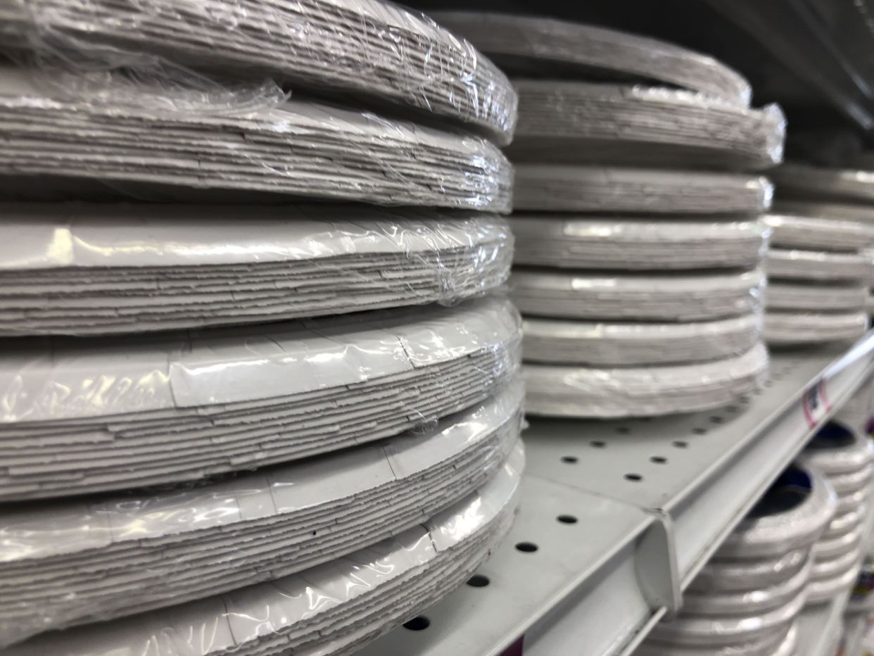 Closeup of a stack of paper plates for sale on a white shelf in a store, with two other stacks beside it, more stacks on a lower shelf