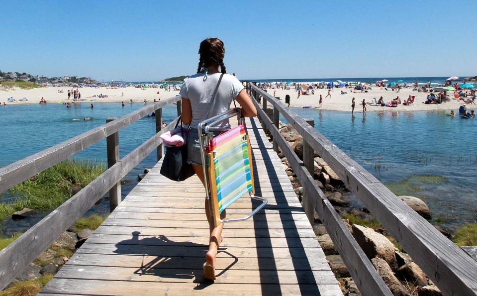File: A beachgoer crosses the footbridge from Nautilus Road to the sands of Good Harbor Beach in Gloucester, Mass.