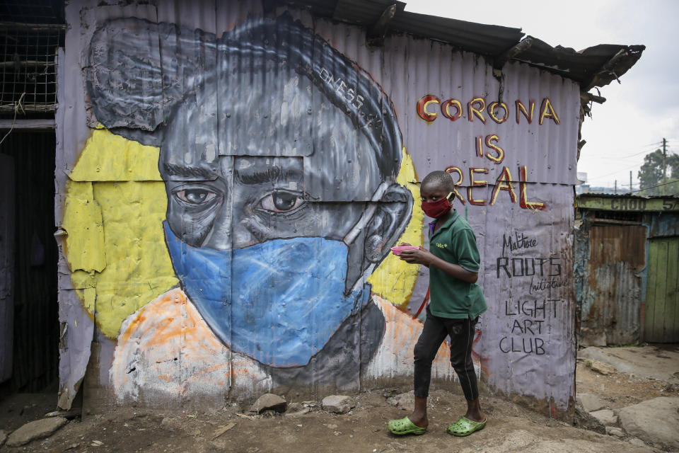 FILE - In this Saturday, April 18, 2020 file photo, a boy wearing a face mask carries a small bowl of "githeri", or mixed beans and maize, for him to eat as he walks past a mural warning people about the risk of the coronavirus, painted by graffiti artists from the Mathare Roots youth group, in the poor Mathare neighborhood of Nairobi, Kenya. As schools reopen in some African countries after months of lockdown, relief is matched by anxiety over everything from how to raise tuition fees amid the financial strain wrought by the COVID-19 pandemic to how to protect students in crowded classrooms. (AP Photo/Brian Inganga, File)