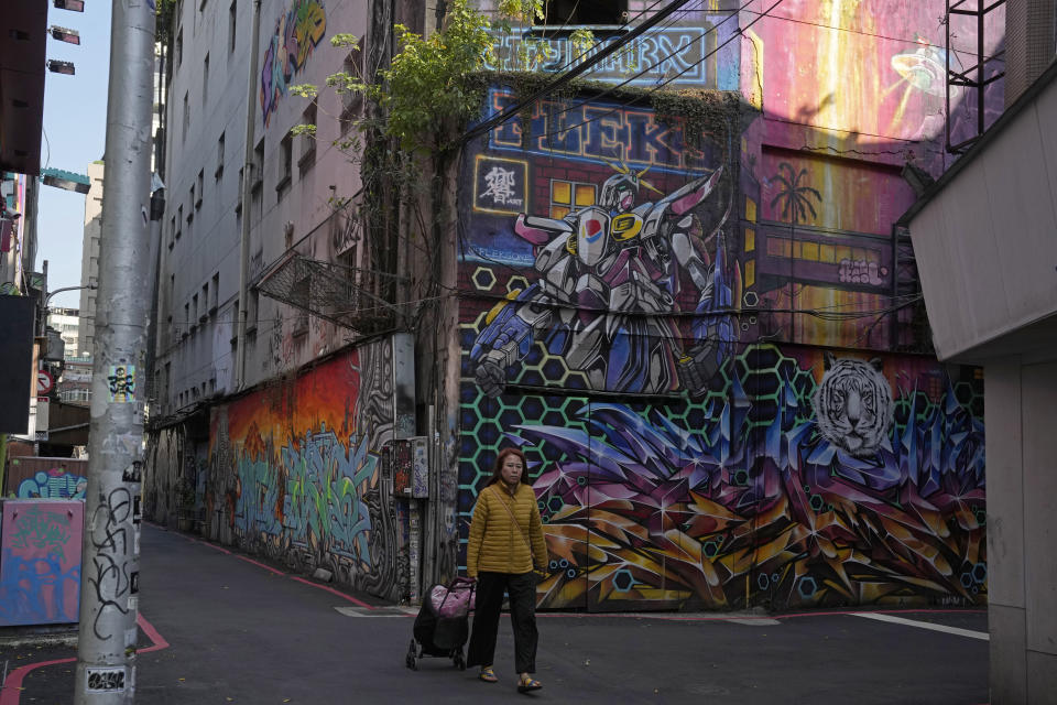 A resident walks past a graffiti in Taipei, Taiwan, Thursday, Jan. 11, 2024. Beijing's threats to use force to claim self-governed Taiwan aren't just about missiles and warships. Hard economic realities will be at play as voters head to the polls on Saturday, though the relationship is complicated. (AP Photo/Ng Han Guan)