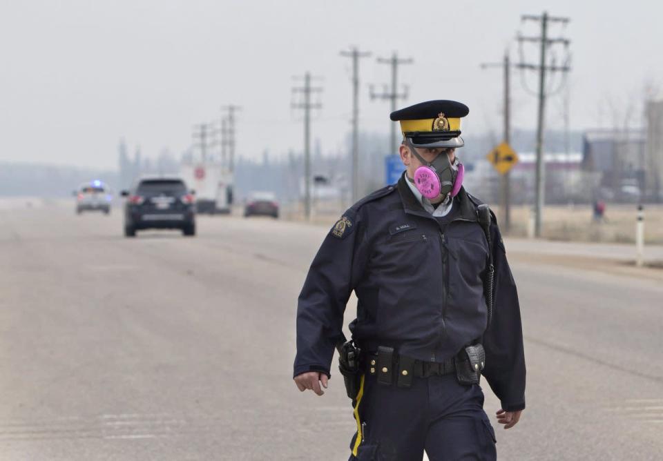 A police officer wears a mask while controlling a roadblock near a wildfire in Fort McMurray, Alta., on Thursday, May 5, 2016. THE CANADIAN PRESS/Jason Franson