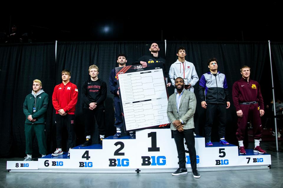 Iowa's Alex Marinelli poses for a photo atop the podium for 165 pounds after scoring a decision in the finals during the third session of the Big Ten Wrestling Championships, Sunday, March 6, 2022, at Pinnacle Bank Arena in Lincoln, Nebraska. As Jordan Burroughs, front right, presents the bracket.