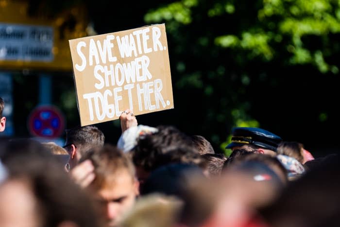 A crowd of people at an outdoor event hold a sign that reads, "Save Water. Shower Together"