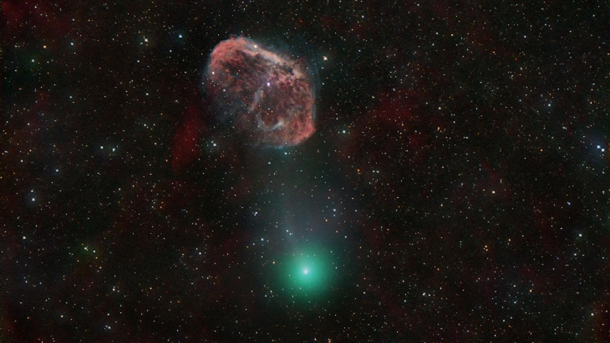  A green comet next to a red, crescent-shaped nebula. 