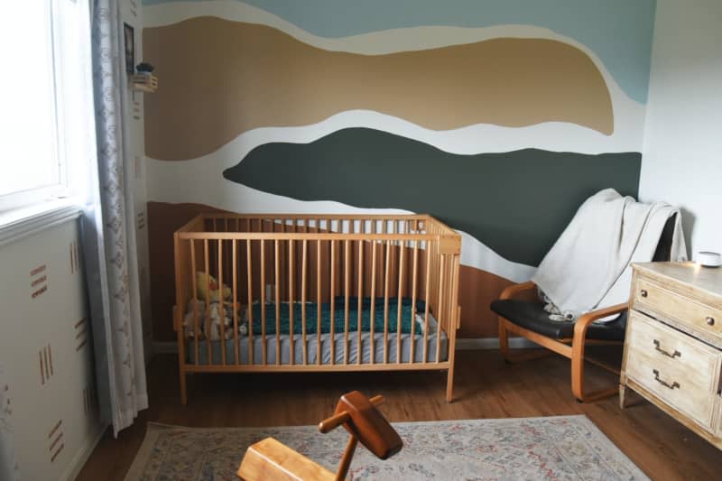 White nursery with gold, blue and green paint and wallpaper design and wood crib