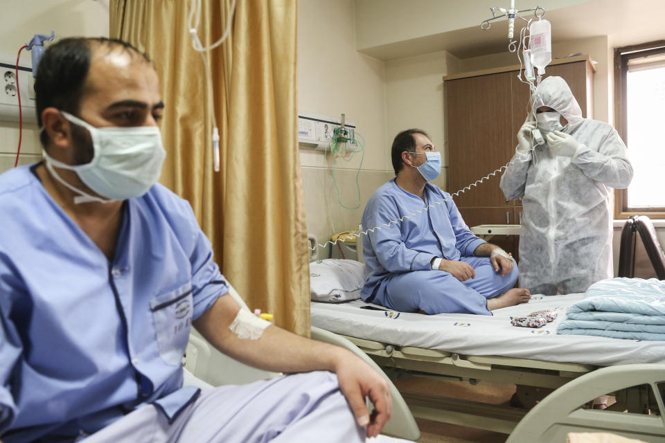 In this Saturday, March 7, 2020, a man wearing protective gear calls on a phone next to the patients in a ward dedicated for people infected with the new coronavirus, at Baqiyatallah Al'Azam Hospital affiliated to the Revolutionary Guard, in Tehran, Iran. Iran is the hardest-hit country in the Mideast by the new coronavirus, which sickens but largely doesn't kill those afflicted. (Mohammad Hasan Zarifmanesh/Tasnim News Agency via AP)