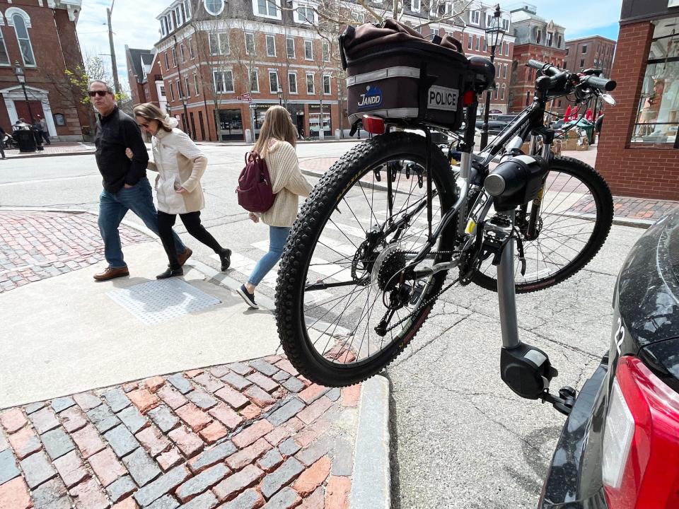 Pedestrians pass a bicycle hanging from a rack attached to a Portsmouth police vehicle in Market Square Monday, April 29, 2024.
