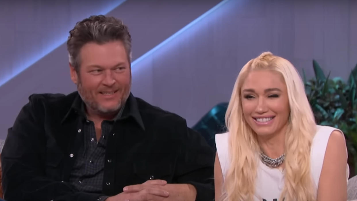  Blake Shelton and Gwen Stefani laughing together on a couch while appearing on The Kelly Clarkson Show. 