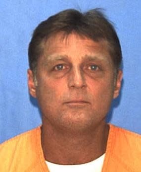 A middle-aged man with short hair wearing an orange shirt poses for a mugshot against a plain background