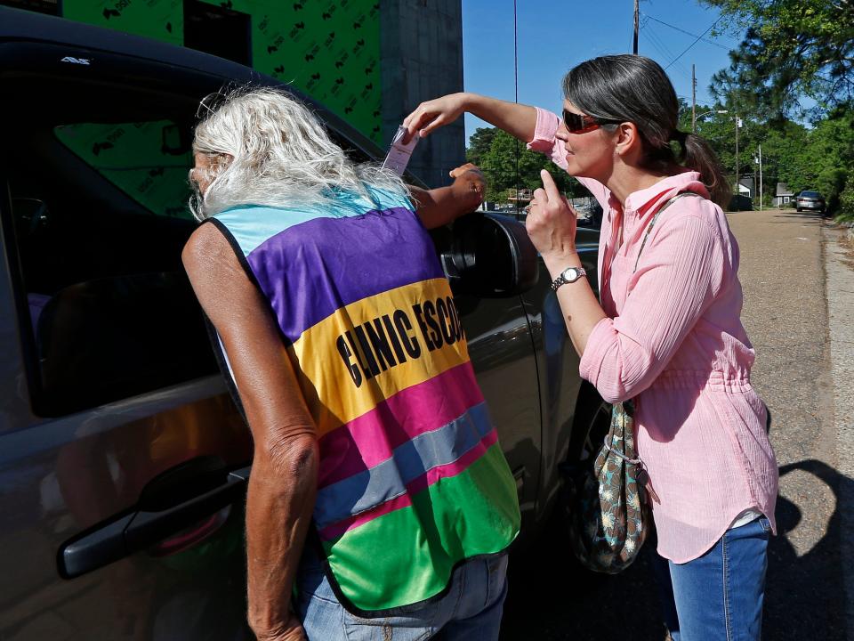 A clinic escort, left, speaks to a driver and patient while an abortion protester attempts to hand over some reading material outside the Jackson Women's Health Organization clinic in Jackson, Miss., Wednesday, April 10, 2019. The clinic is the only medical facility that performs abortions in the state. The state legislature recently passed a law that would ban most abortions after a fetal heartbeat is detected, meaning as early as six weeks.