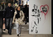 People walk past a street art image by Rich Simmons portraying Britain's Queen Elizabeth II spray painting the words "Will + Kate" in a love heart outside the Opera Gallery in London, April 1, 2011. (AP Photo/Matt Dunham)