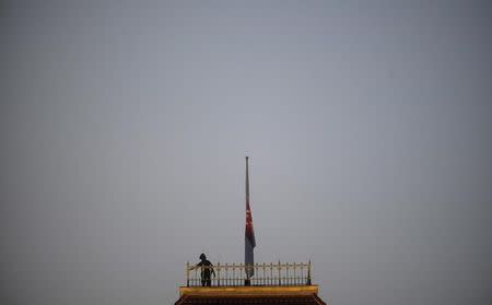 A policeman looks at the state flag after lowering it to half-mast at the Parliament building in Singapore March 23, 2015. REUTERS/Timothy Sim