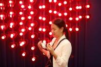 A woman removes her protective masks to take a selfie in front of hearts celebrating Valentine's Day in a skytrain BTS station in Bangkok