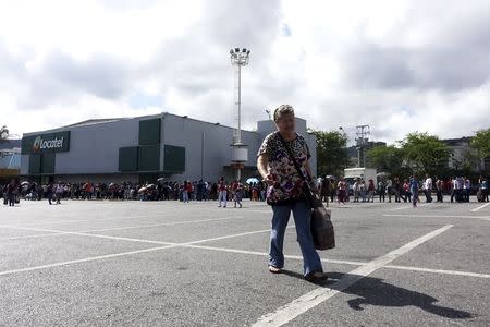 A woman carries a plastic bag as people queue to purchase staple items at a Makro supermarket in Caracas August 4, 2015. REUTERS/Carlos Garcia Rawlins