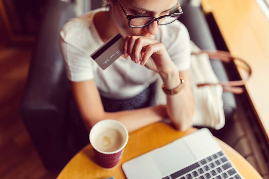A woman sits at a cafe on her laptop with coffee while holding her credit card. 