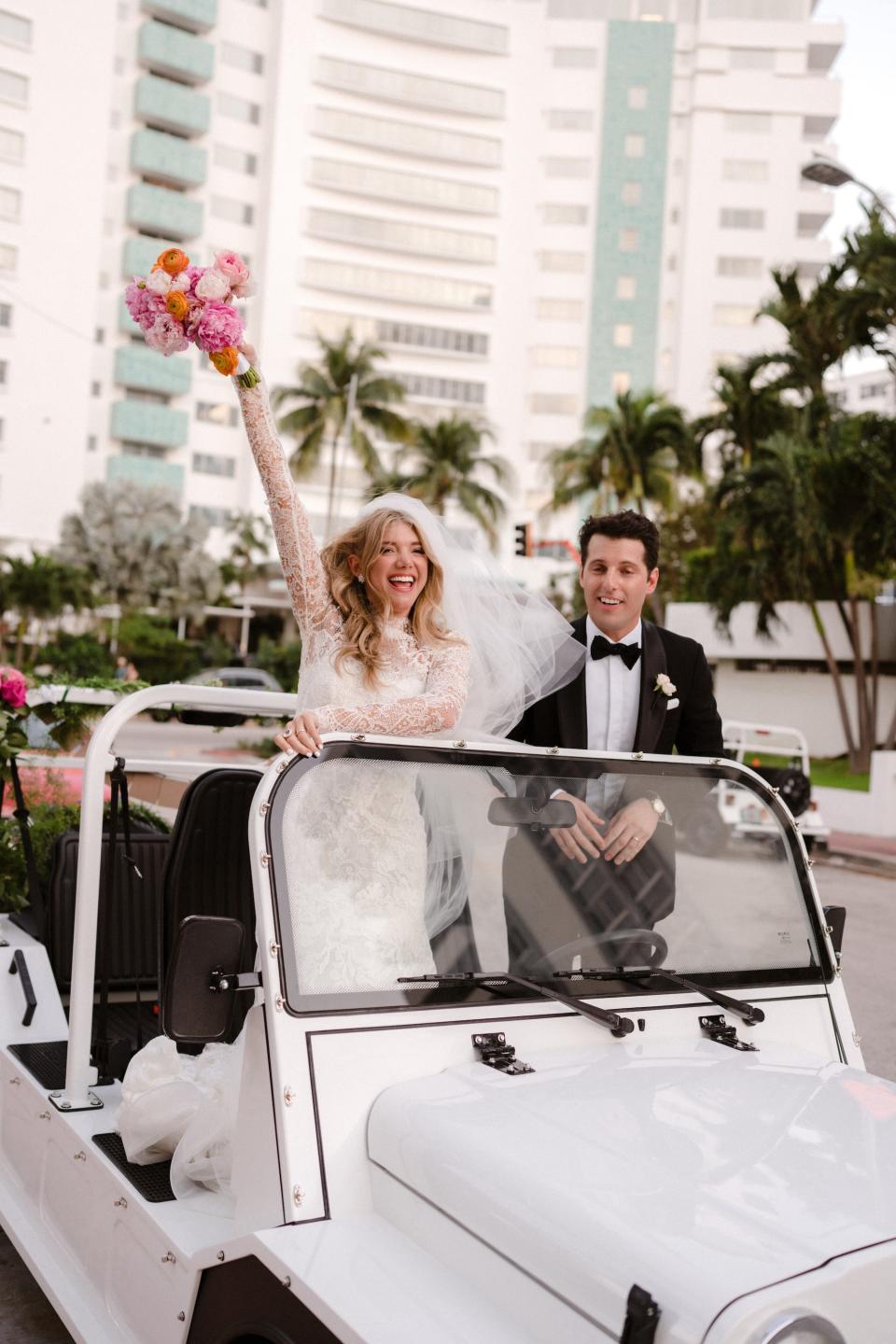 A bride and groom stand in a white open top jeep.