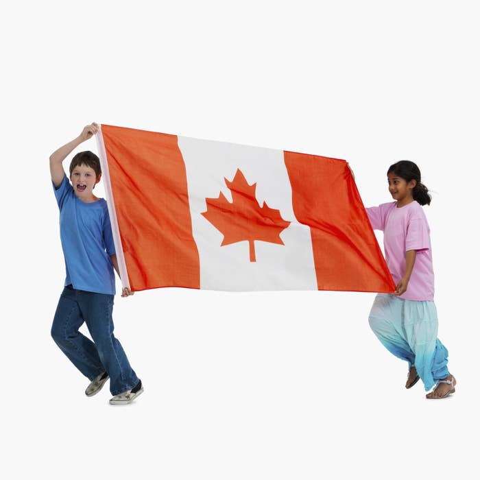 Two children holding up a large Canadian flag