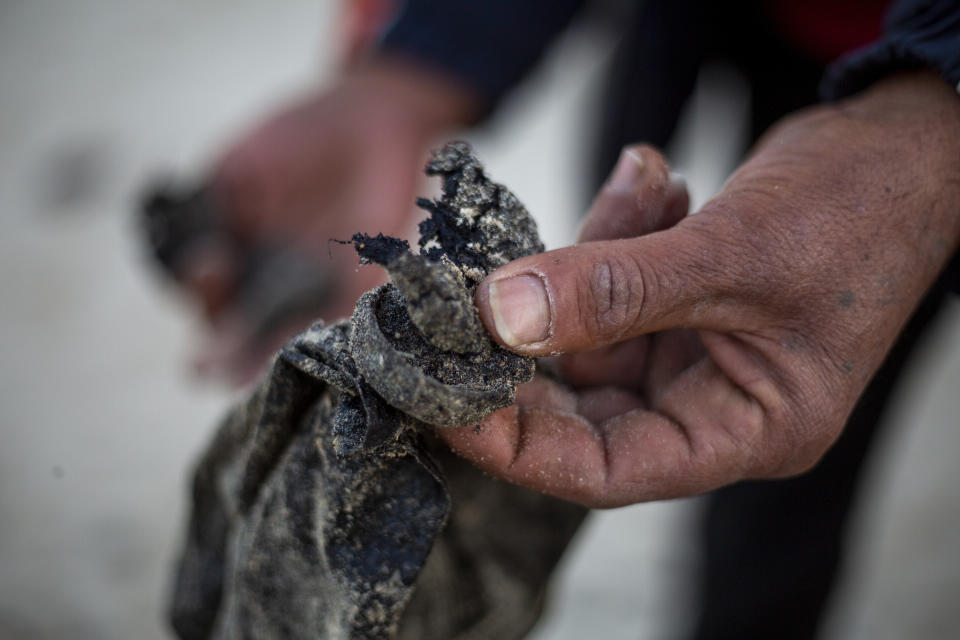 A local fisherman who goes by the name Jumbo holds tar that washed on to the docks from an oil spill in the Mediterranean Sea, in the Israeli Arab village of Jisr al-Zarqa, Israel, Thursday, Feb. 25, 2021. After weathering a year of the coronavirus pandemic, an oil spill in the Mediterranean whose culprits remain at large delivered another blow for the fishermen of Jisr al-Zarqa. (AP Photo/Ariel Schalit)