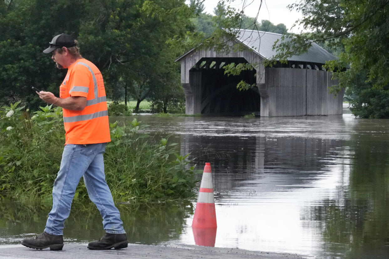 A man in an orange vest walks by a flooded river.