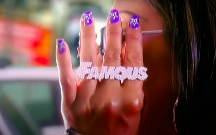a woman adjusting her glasses and wearing a ring that says "Famous"