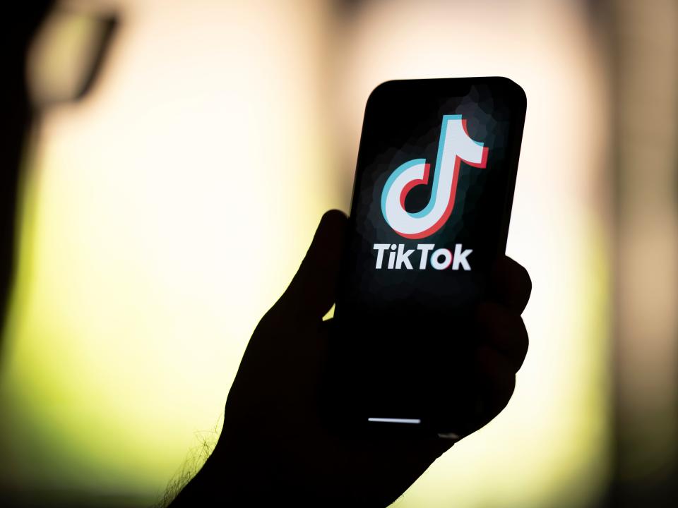 A silhouette of a hand holding a phone with Tik-Tok on the screen.