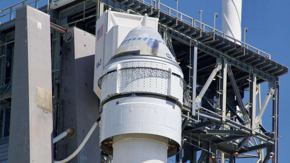 A space capsule atop a rocket ship rests against a launch tower.