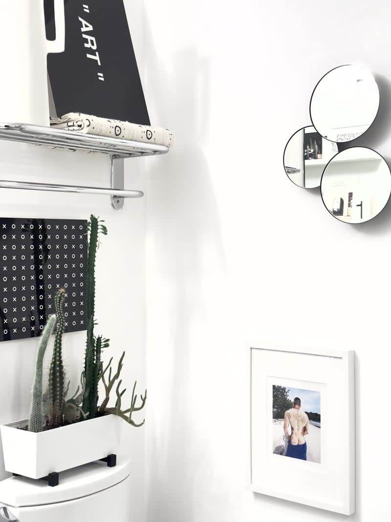 Catus atop a toilet next to a framed photo in a white-walled bathroom.