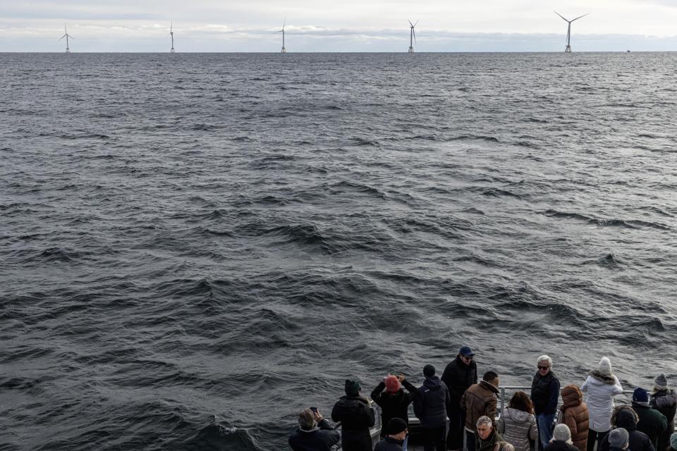 FILE - Guests observe the five turbines of America's first offshore wind farm, Block Island Wind Farm, Dec. 7, 2023, off the coast of Block Island, R.I., during a tour of the South Fork Wind farm organized by Orsted. Unfounded claims about offshore wind threatening whales have surfaced as a flashpoint in the fight over the future of renewable energy. (AP Photo/Julia Nikhinson, File)