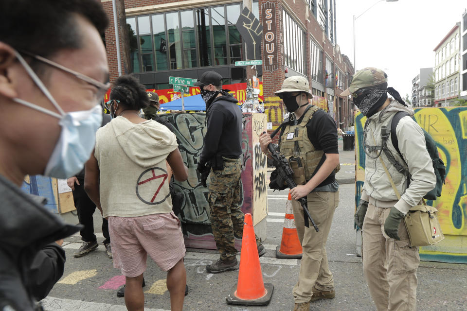 A person who said he goes by the name James Madison, second from right, carries a rifle as he walks Saturday, June 20, 2020, inside what has been named the Capitol Hill Occupied Protest zone in Seattle. Madison is part of the volunteer security team who have been working inside the CHOP zone, and said he and other armed volunteers were patrolling Saturday to keep the area safe. A pre-dawn shooting Saturday near the area left one person dead and critically injured another person, authorities said Saturday. The area has been occupied by protesters after Seattle Police pulled back from several blocks of the city's Capitol Hill neighborhood near the Police Department's East Precinct building. (AP Photo/Ted S. Warren)