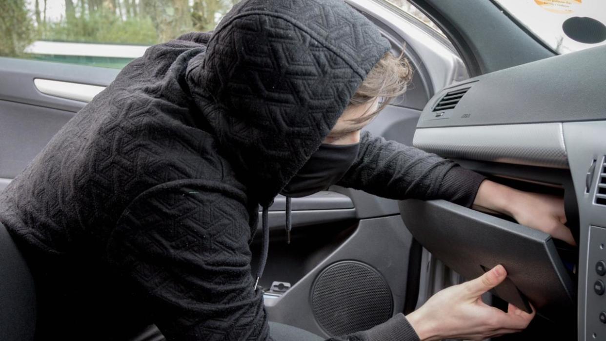 Masked teenage criminal stealing from a car