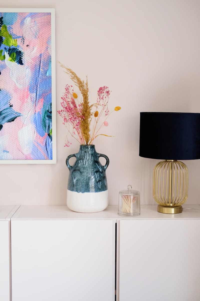 white cabinets with white frame tv and black lamp shade on gold lamp base, teal and white vase with flowers