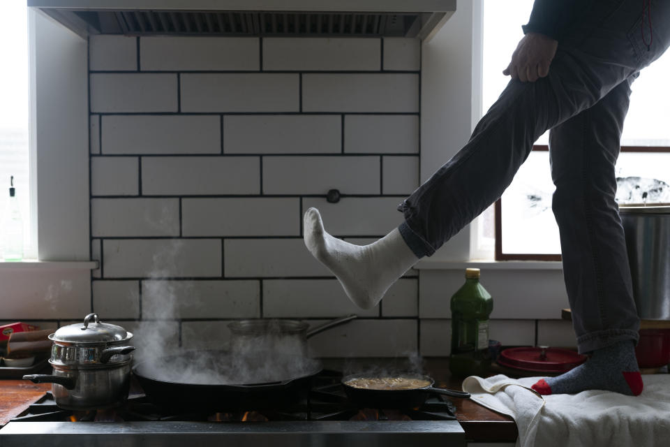 Jorge Sanhueza-Lyon stands on his kitchen counter to warm his feet over his gas stove Tuesday, Feb. 16, 2021, in Austin, Texas. Power was out for thousands of central Texas residents after temperatures dropped into the single digits when a snow storm hit the area on Sunday night. (AP Photo/Ashley Landis)